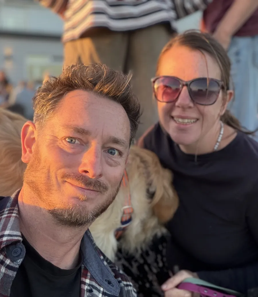 Jason from PureClean smiling in the evening sun, with a woman in sunglasses and their dogs